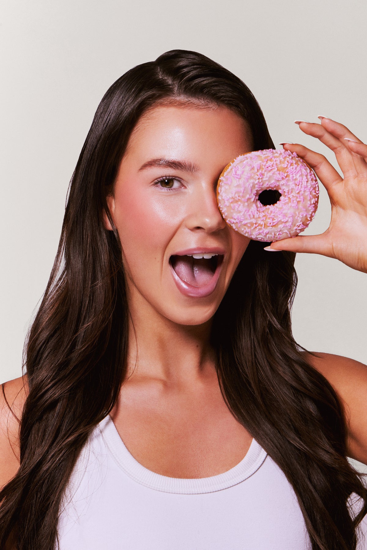 Woman holding a pink donut up to her eye against a plain background