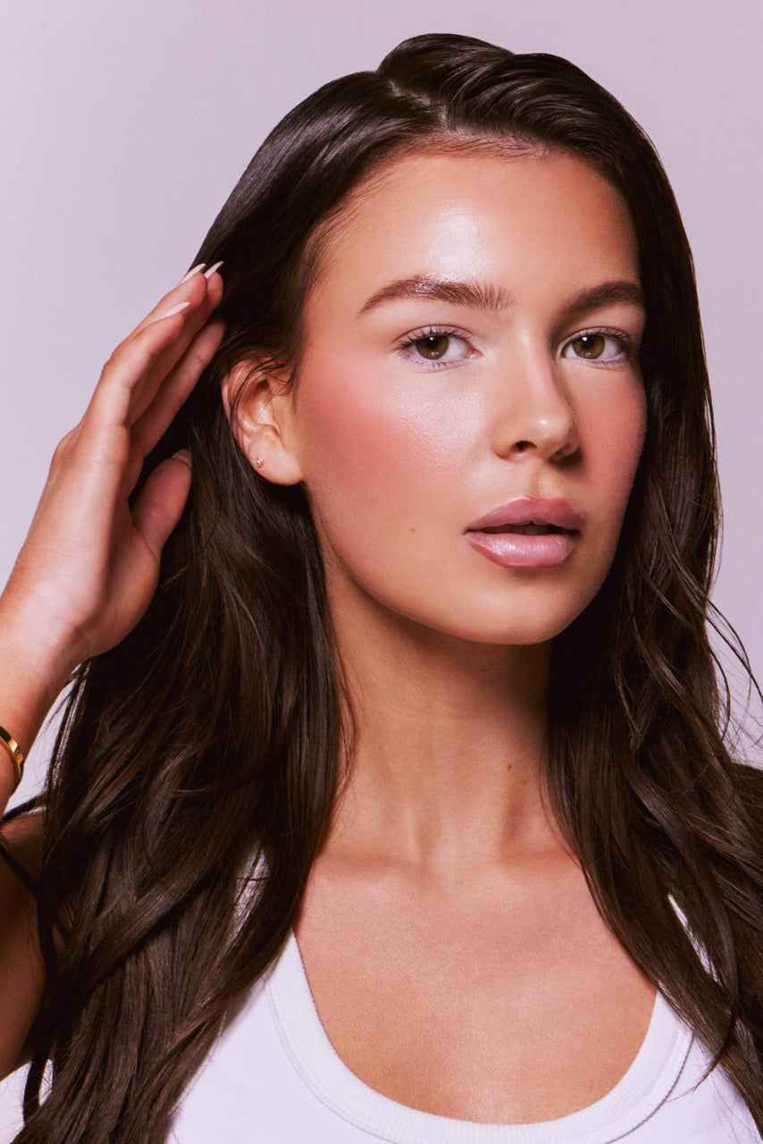 Woman with long brown hair touching her head against a light purple background