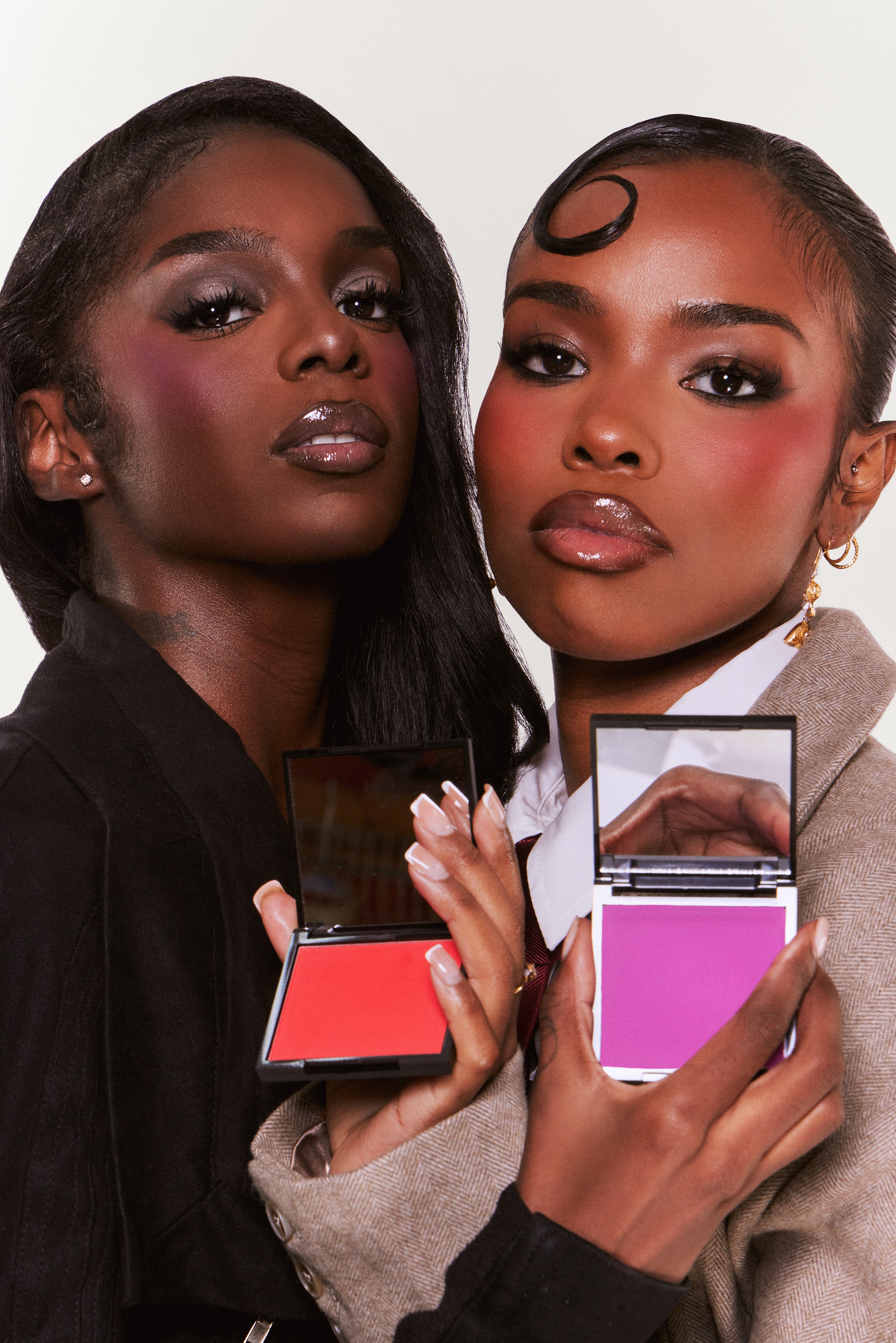 Two women holding makeup products with a neutral background