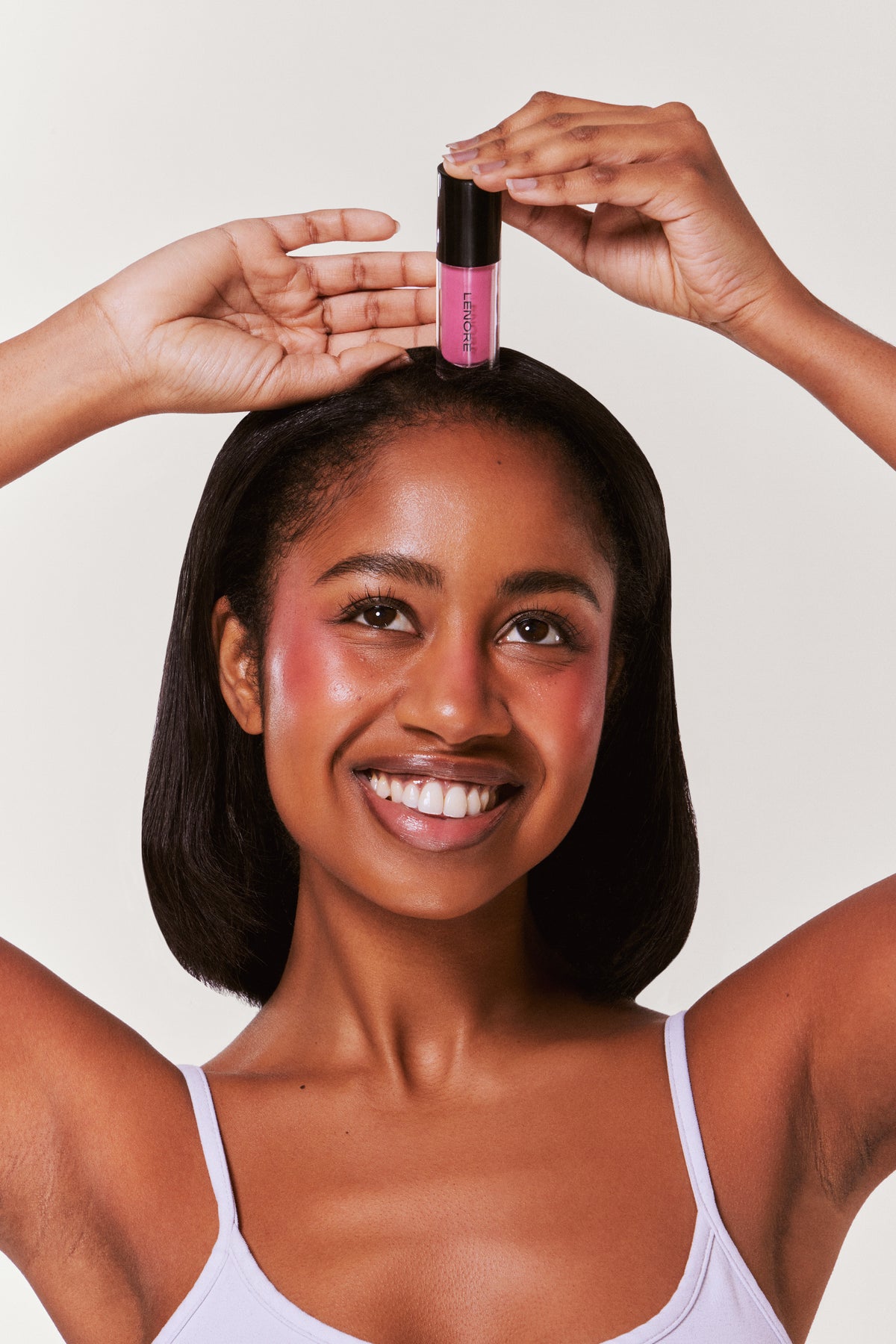 Woman holding a pink bottle above her head with a plain background