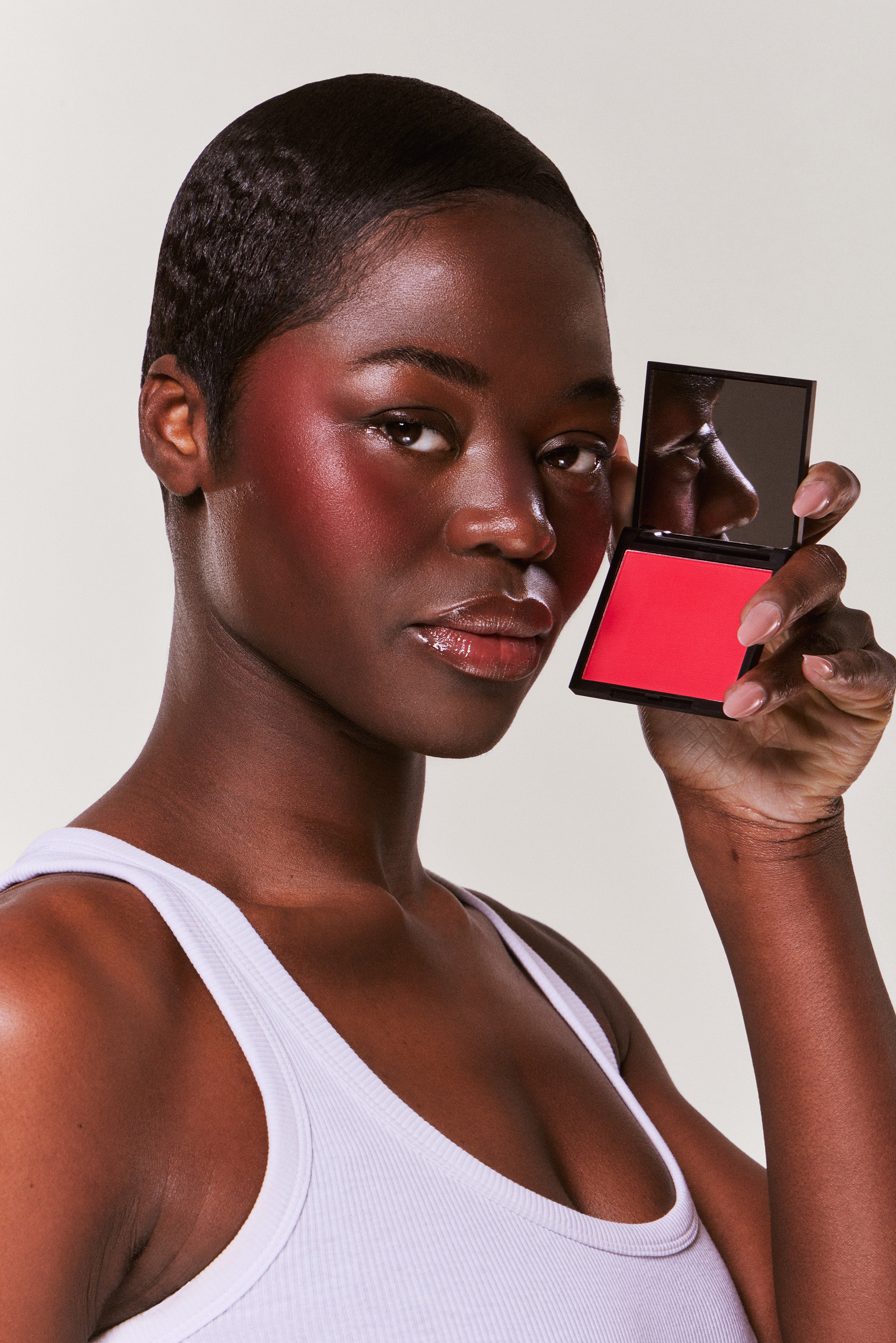 Woman holding a makeup compact with a red blush on a plain background