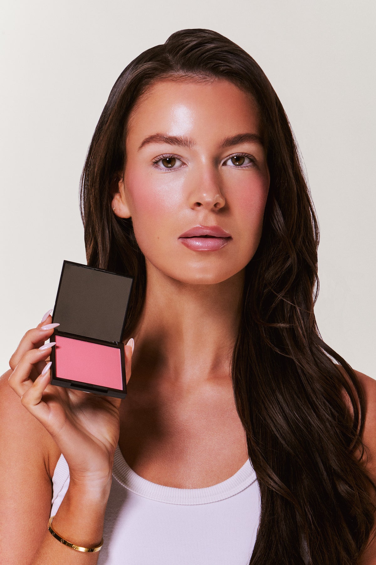Woman holding a makeup compact with pink blush on a plain background