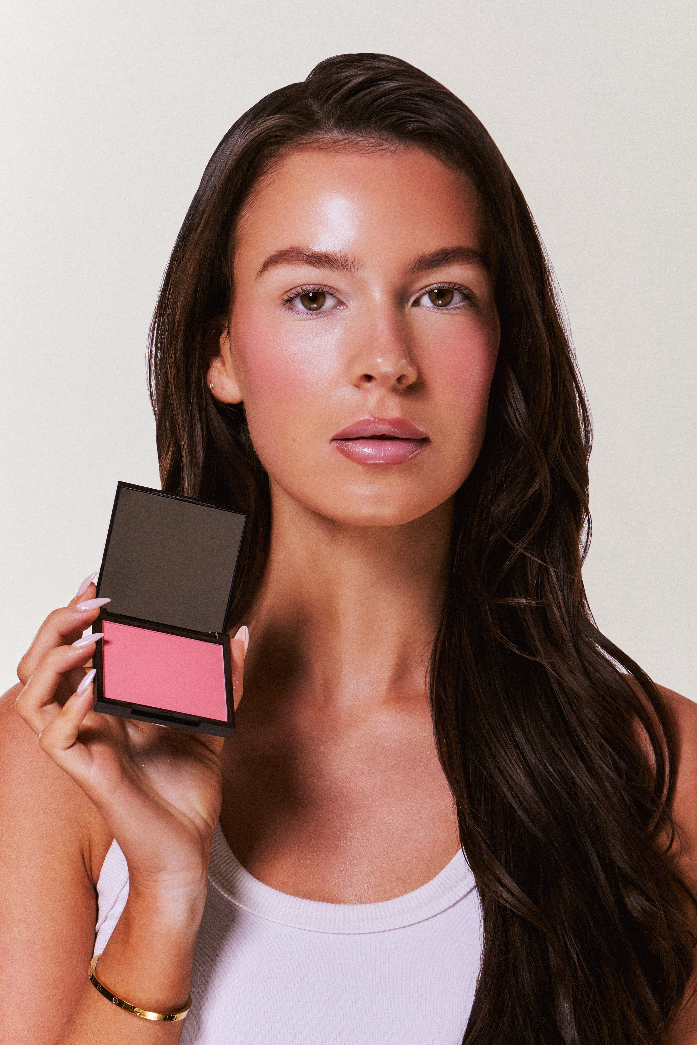 Woman holding a makeup compact with pink blush on a plain background