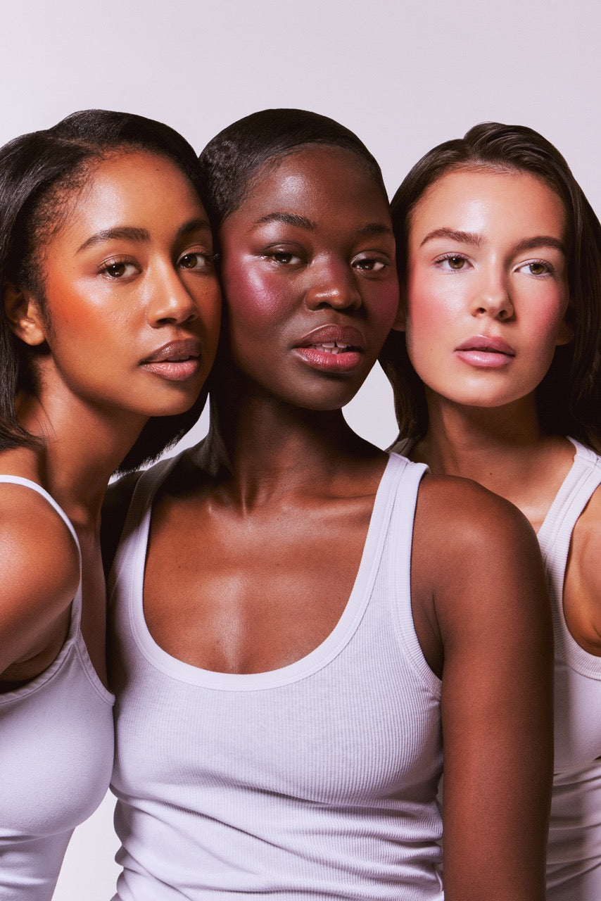 Three women wearing white tank tops against a light background