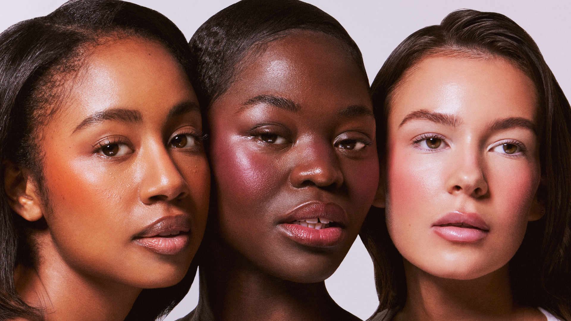 Three women with different skin tones standing close together against a white background